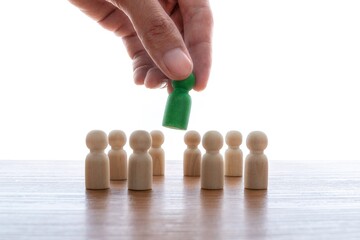 A hand picking up a green peg doll from a group of wooden peg dolls. Selection, leadership, hiring,...