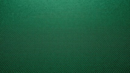 Close up view of an emerald green textile with a repeating diagonal pattern in a dark environment