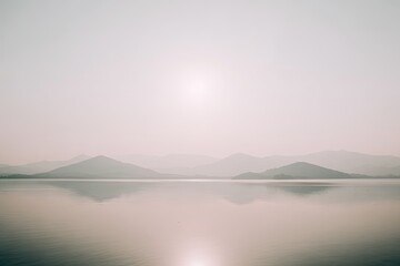 Misty lake sunrise over mountains. Soft light reflects on still water