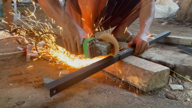 A construction worker uses an angle grinder to cut metal, producing bright sparks.