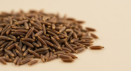 Macro photograph of a pile of aromatic whole cumin seeds on a neutral beige background, showcasing their texture and detail.