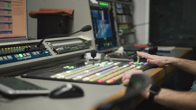 Close-up of hand operating video production switcher in broadcast studio. Professional television equipment with illuminated buttons and monitor in control room environment