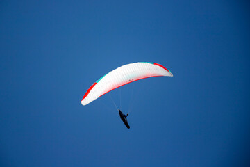 A man with a paraglider in front of a blue sky.