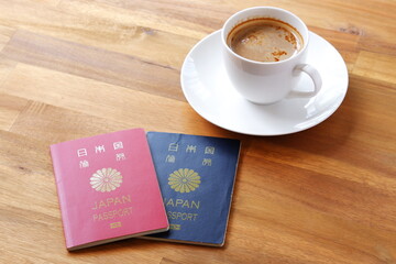 パスポート（10年用赤色と5年用紺色）を用意して、コーヒーを飲みながら海外旅行を計画しているイメージ
