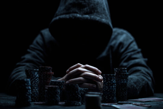 Mysterious gambler in a hoodie with a stack of poker chips at a table in a dimly lit room.