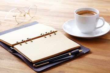 Opened schedule planner, diary, notebook with cup of Coffee on table
