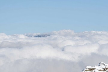 High-altitude view of puffy white clouds, with a distant mountain peak