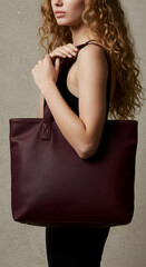 Woman holding a deep burgundy tote bag against a neutral backdrop