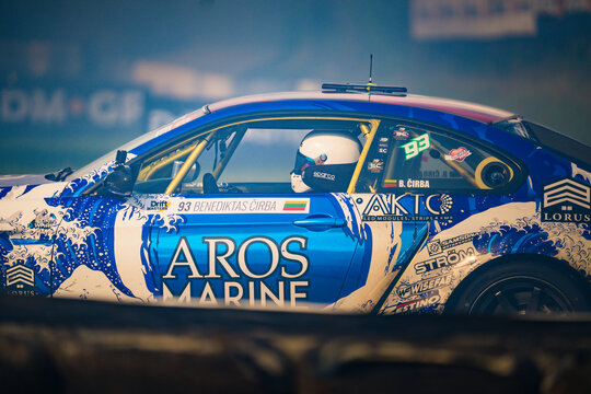 Speeding through the night, the 'AROS MARINE' race car, adorned with sponsor logos like 'AKTC' and 'LORUS', cuts a dynamic figure against the blurred backdrop of a racing track