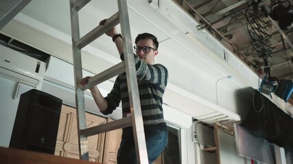 studio worker climbing ladder adjusting lighting SL-200W, preparing for broadcast production, adjusting equipment for proper lighting in a professional studio environment, production setup