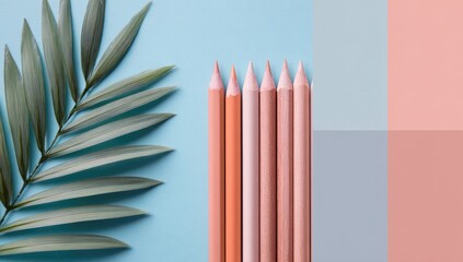 Pastel colored pencils stand upright against a pale blue background, next to a single, delicate palm frond.  A color-blocked backdrop of light blue, grey and peach completes the image