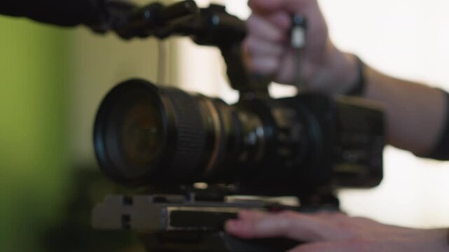 cameraman's hand adjusting camera in film production, close-up shot capturing detailed focus on lens, filming setup in studio, video production in progress, professional crew at work