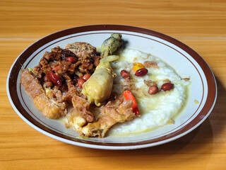 A dish of chicken porridge with yellow sauce, chicken pieces, omelet, orek tempeh and fried peanuts, served on a brown enamel plate. Chicken porridge, traditional Indonesian food.