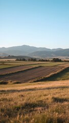 Obraz premium Scenic Farmland Landscape with Mountains in the Background at Sunset