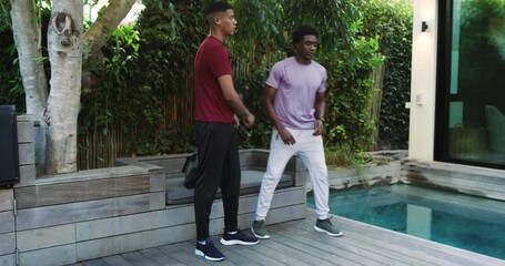 Diverse male friends stepping on deck tying shoelaces stretching doing push-ups by pool for fitness - Powered by Adobe