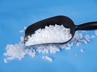 Black plastic scoop overflowing with dry ice pellets scattered on blue background