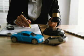 A lawyer uses a gavel near a toy car, symbolizing legal proceedings, car insurance claims, court...