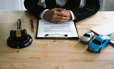 A lawyer uses a gavel near a toy car, symbolizing legal proceedings, car insurance claims, court...