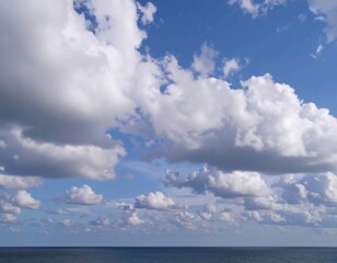 Expansive blue sky filled with fluffy cumulus clouds above a calm, dark blue ocean horizon