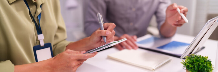 Adult business professionals collaborate discussing project ideas taking notes using pen notebook and digital tablet stylus in modern office workspace for effective planning
