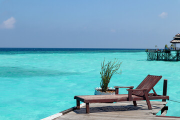 A wooden deck with lounge chairs and small potted plants. Overlooking the clear turquoise sea