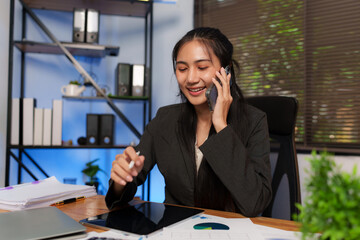 Asian businesswoman sits using a smartphone to work on documents.