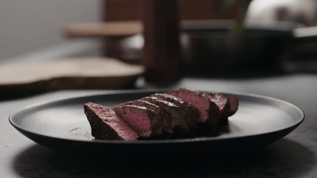 Slow motion orbit shot of sliced beef steak on black plate on concrete countertop
