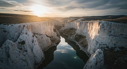 Aerial view of a canyon with white cliffs and a river reflecting the sky at sunset in the desert