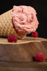 one ice cream lies on a walnut board close up, ripe red raspberries and raspberry cold natural ice cream on the table