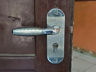Close-up of worn chrome door handle and lock on a brown wooden interior door