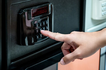 Hand try to press button on modern keypad lock on safe at home decor store. Customer choosing security cabinet with digital display for valuables storage. Entering password number to unlock secure box