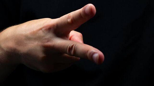 Rock paper scissors game on black background.
Man showing scissors in game.
Male hand imitating scissors in dark room
