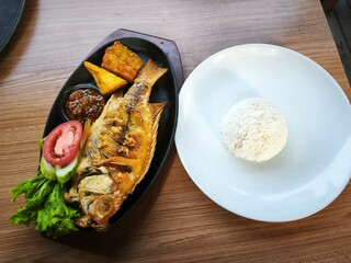 Delicious traditional Indonesian fried fish served with steamed rice, sambal, fresh vegetable, tempeh, and tofu on a wooden table – perfect for Asian food lovers.