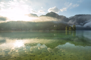 Naklejka premium Mystischer Morgen am Königssee in Schönau mit Bootshäusern und Christlieger. Sonnenaufgang und schöne Nebelschwaden über dem Königssee im Kessel.