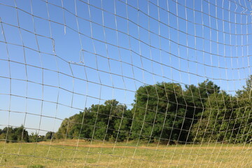 Damaged football goal net with a noticeable tear, captured on a quiet field. The beauty of...