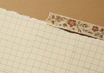 Torn grid paper with vintage floral decorative tape on a textured background