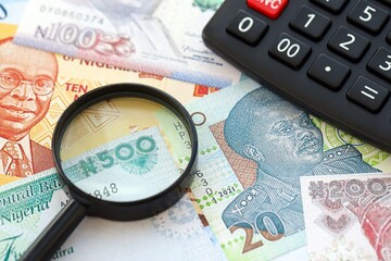 Nigerian naira currency money bills and calculator with magnifying glass. The concept of taxation and money count