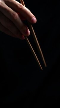 chopsticks on a black background in the hands of an Asian man.
Chopsticks for sushi and sashimi are used.
Japanese traditional chopsticks large stick in the hands of a man