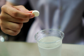 Hand Holding Effervescent Tablet Over Glass of Water