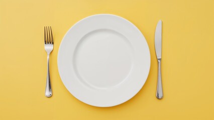 Cutlery consisting of a knife and fork placed near a white dish on a yellow background.
