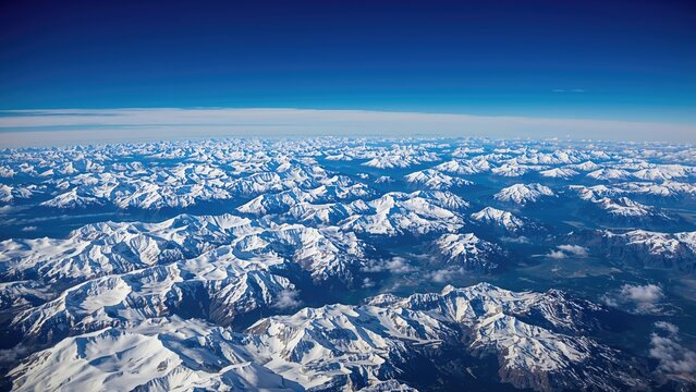 An impressive bird's-eye snapshot of towering snowy mountains and ice formations reaching out to the distant horizon, mirroring the azure sky.