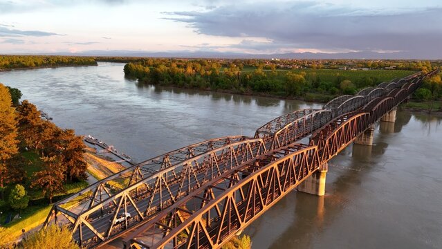 Sunset illuminating historic Iron Bridge crossing Fraser River, verdant landscape and misty mountain range framing picturesque scene near Chilliwack, British Columbia