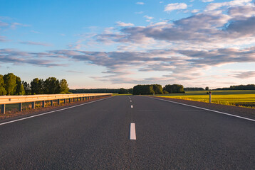 Endless asphalt road stretching through lush green fields under open blue sky