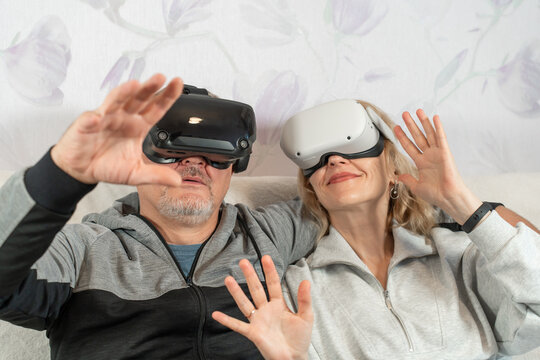 Smiling Man and Woman Using Virtual Reality Headsets for Fun Time on Living Room Sofa. Mature Man and Woman Wearing VR glasses.