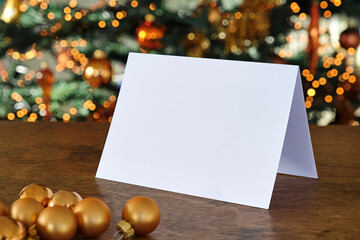 Standing blank empty rectangular greeting card mock up with Christmas balls and before a blurred christmas tree with copy space. For use as a Christmas background template.	