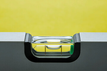 Close-up of grey metal spirit level with bubble against a yellow background. Image with copy space....