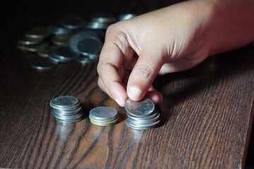A female hand placing or stacking coins on a wooden surface