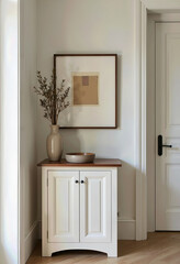 Fototapeta premium A charming and rustic hallway vignette featuring a white painted cabinet topped with a framed art print and a simple vase of dried flowers under soft, natural light. 