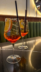 Effervescent Aperol Spritz glasses glisten under soft lights, evoking Aperitivo Hour in Venice,...