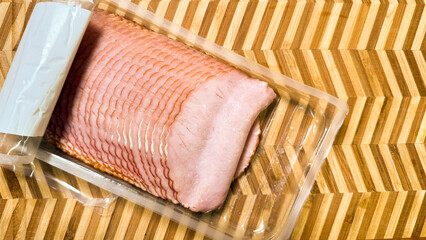 Sliced ham in vacuum-sealed embrace, echoing Salt Awareness Week, charcuterie artistry, culinary symphony on patterned wooden stage